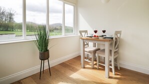 A dining area with a table, chairs, and a view of a green landscape through large windows. - Glen Cottage (Penrith)