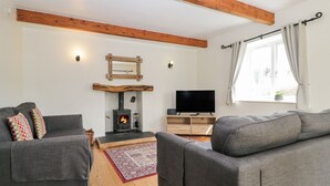 A living room with a fireplace, two grey sofas, a television, and a window with curtains. - Glen Cottage (Penrith)