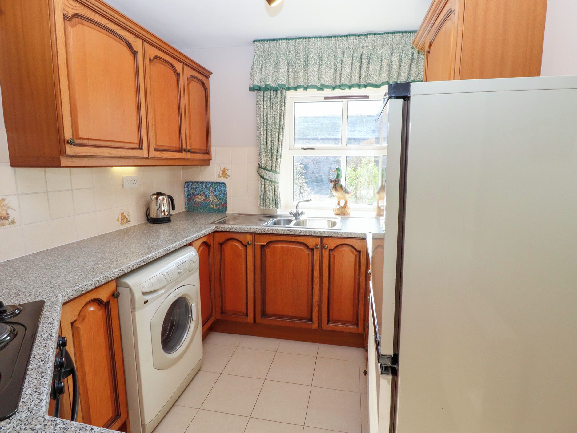 A compact kitchen with wooden cabinets, a washing machine, a sink, and a window with a view.