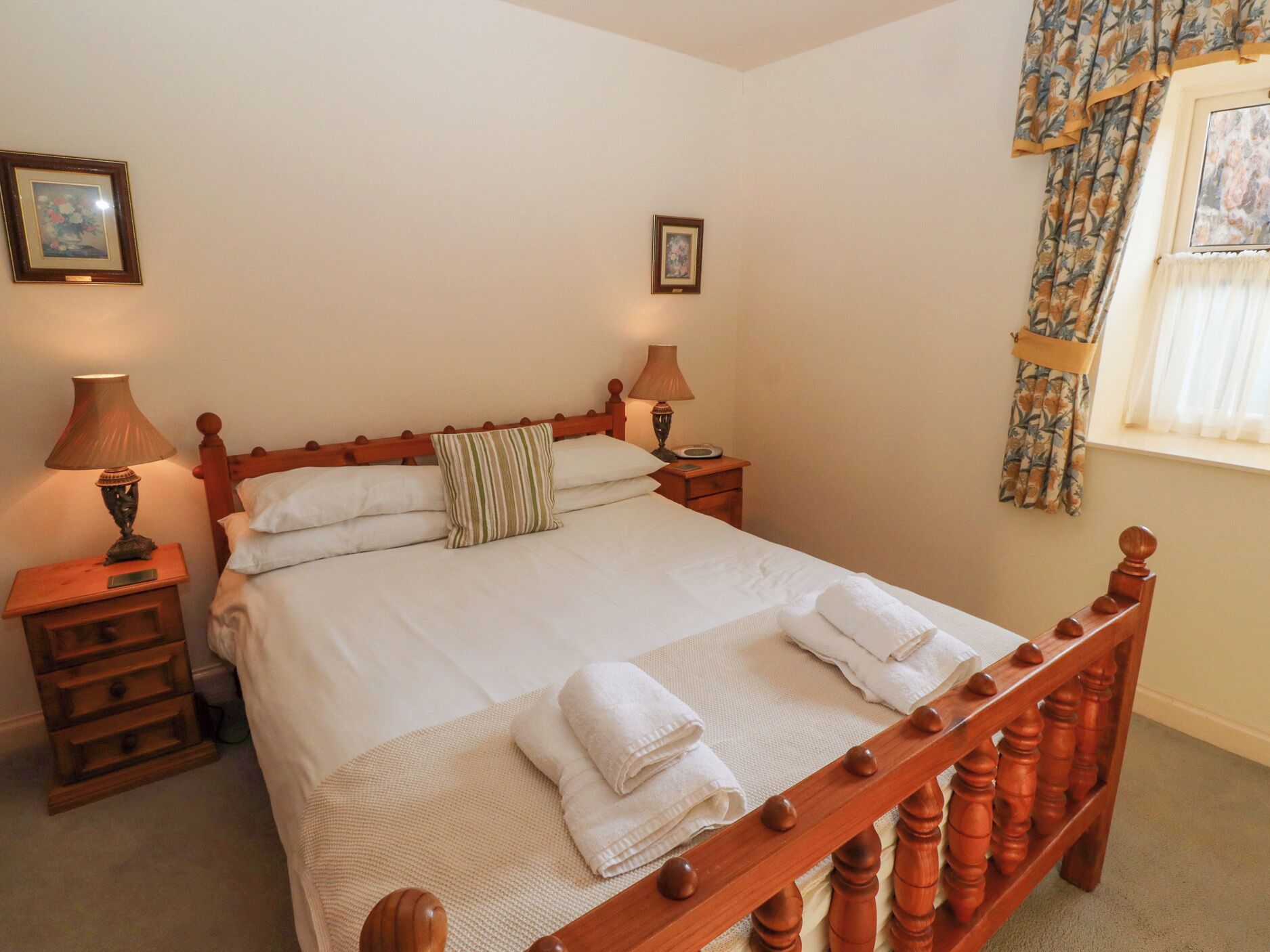 A neatly made bed with white linens and two pillows, flanked by wooden nightstands with lamps.