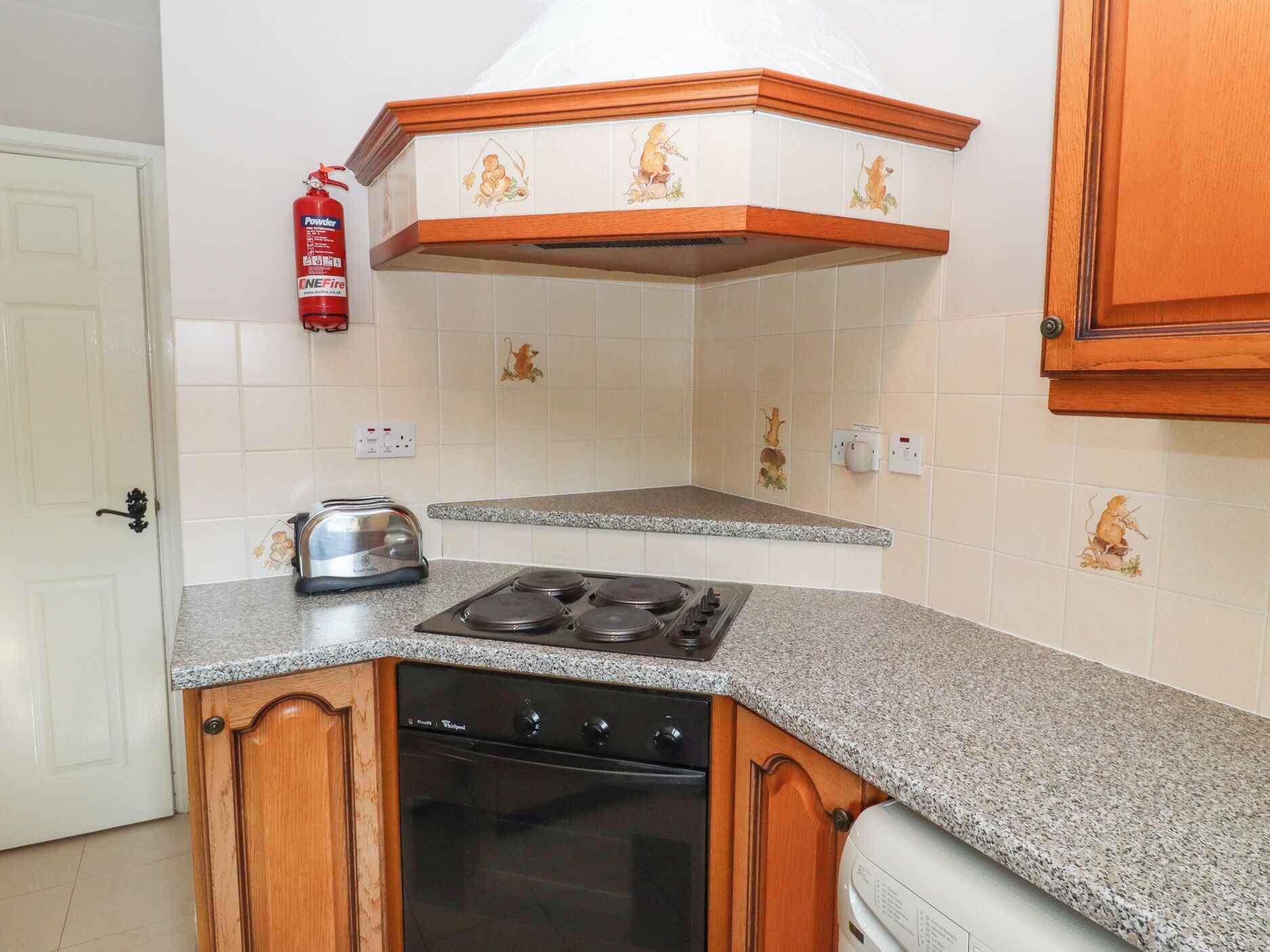 A kitchen with a stove, oven, and toaster. There is a fire extinguisher on the wall.