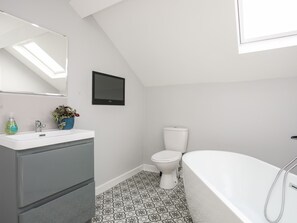 A modern bathroom with a white sink, mirror, and toilet, a bathtub, and a patterned floor. - Twyni Mawr (Rhosneigr)