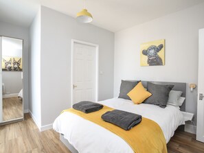 A modern bedroom with a bed, a yellow throw blanket, and a painting of a dog. - Twyni Mawr (Rhosneigr)