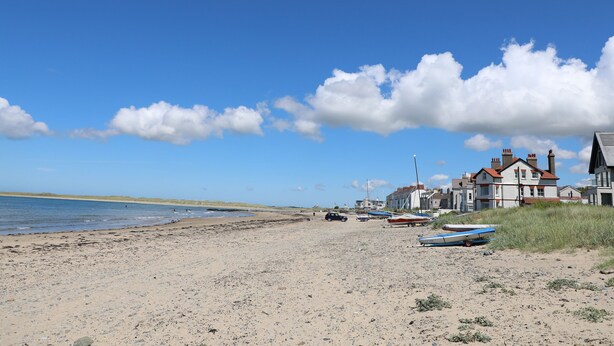 Ein Sandstrand mit Booten, einem klaren blauen Himmel und Häusern im Hintergrund.