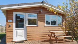 A wooden cabin with two windows, a door, and a picnic table on a wooden deck. - 224 Atlantic Bays (Padstow)