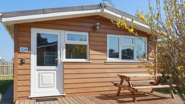 A wooden cabin with two windows, a door, and a picnic table on a wooden deck. - 224 Atlantic Bays (Padstow)