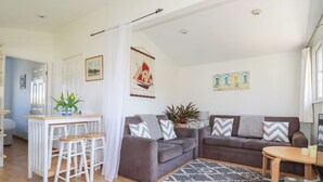 A modern living room with a grey sofa set, a small dining table with stools, a grey patterned rug, and a white curtain. - 224 Atlantic Bays (Padstow)