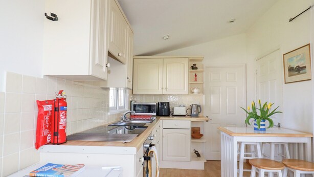 A compact kitchen with white cabinets, a microwave, a kettle, and a small dining area with stools. - 224 Atlantic Bays (Padstow)