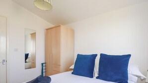 A neatly made bed with blue pillows and rolled towels, a wooden wardrobe, and a mirror on the wall. - 224 Atlantic Bays (Padstow)