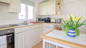 A kitchen with white cabinets, a microwave, a kettle, and a vase with yellow tulips. - 224 Atlantic Bays (Padstow)