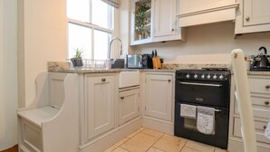 Une cuisine avec des meubles blancs, une cuisinière noire et une fenêtre agrémentée d’une lambrequin.