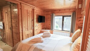 En stuga med träpanel, ett rum med en säng, en tv som är monterad på väggen och ett fönster med gardiner.