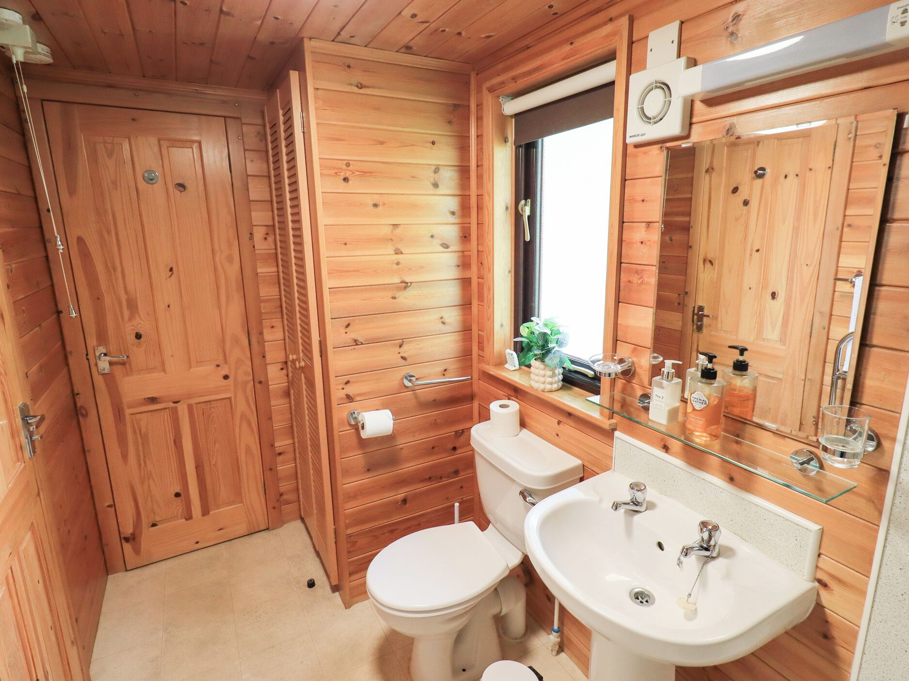 A wooden-paneled bathroom with a toilet, sink, and mirror.