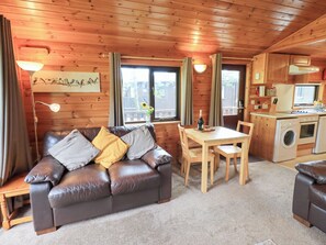 A cozy cabin interior with a leather sofa, wooden dining table, and a kitchenette with a washing machine. - Squirrels Leap (Keswick)