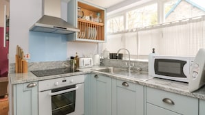 Une cuisine moderne avec des meubles de couleur bleu clair, un four encastré, un four à micro-ondes et une fenêtre donnant sur les arbres.