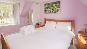 Une chambre à coucher avec un grand lit, une table de chevet, une commode, une fenêtre avec des rideaux et un tableau au mur.