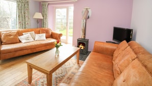 A living room with a sofa, a coffee table, a television, and a wood-burning stove. - Puccini (Pitlochry)