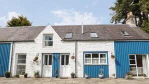 A white building with blue accents, a tiled entrance, and potted plants. - Puccini (Pitlochry)