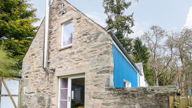 A stone building with a blue exterior, a white bench, and a door leading to a patio area. - Puccini (Pitlochry)