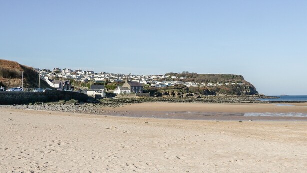 A sandy beach with a rocky shoreline, a small town with white houses, and a cliff in the background. - 3 Parc Delfryn (Brynteg)