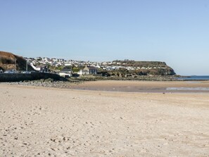 Une plage de sable bordée d’une côte rocheuse, une petite ville aux maisons blanches et, au loin, une falaise.