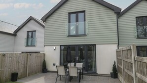 A two-story house with a patio area featuring a table and chairs. - 3 Parc Delfryn (Brynteg)