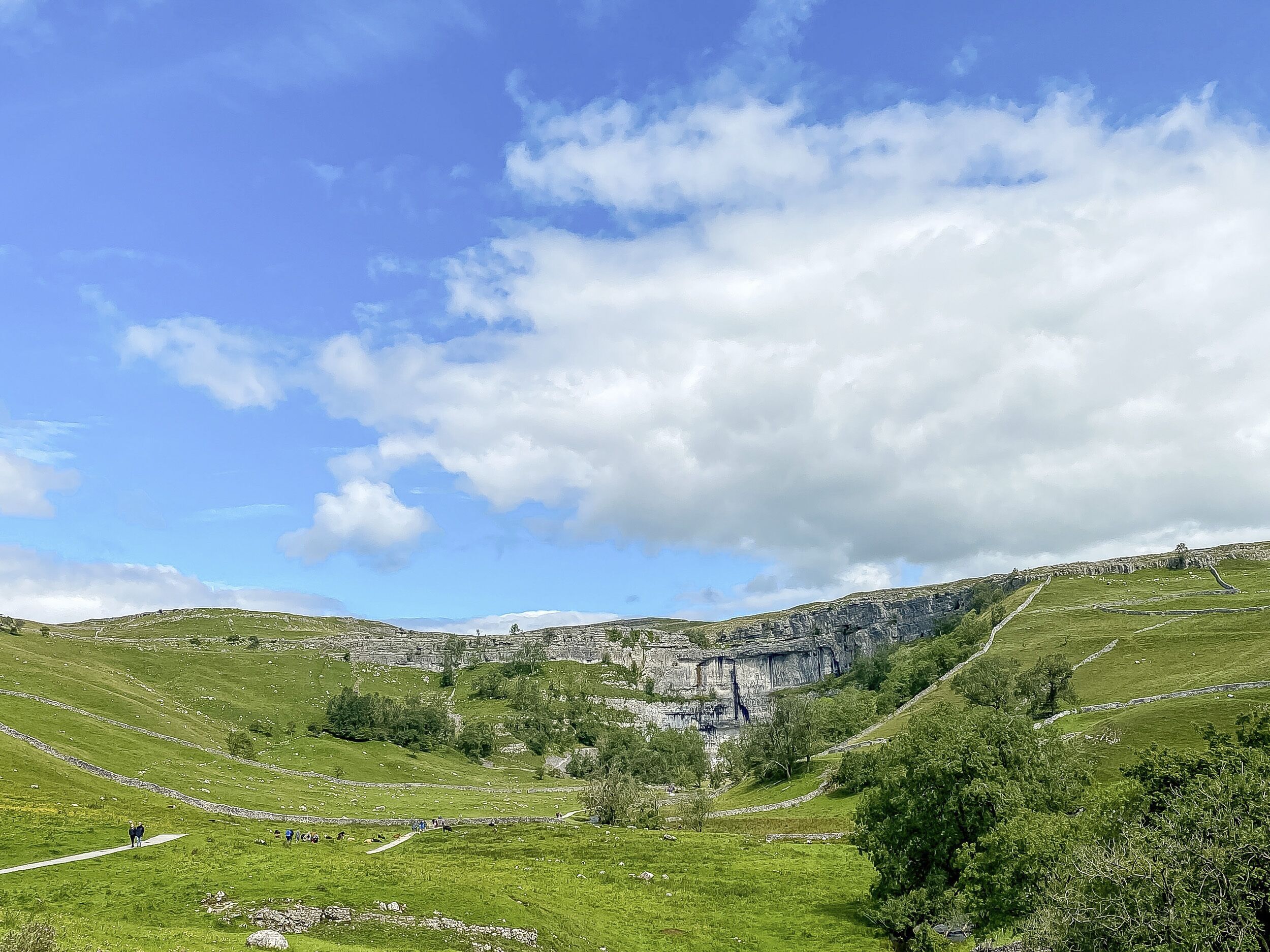 A panoramic view of a lush green valley with a prominent cliff face and a waterfall.