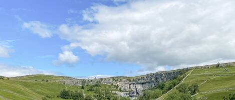 A panoramic view of a lush green valley with a prominent cliff face and a waterfall.