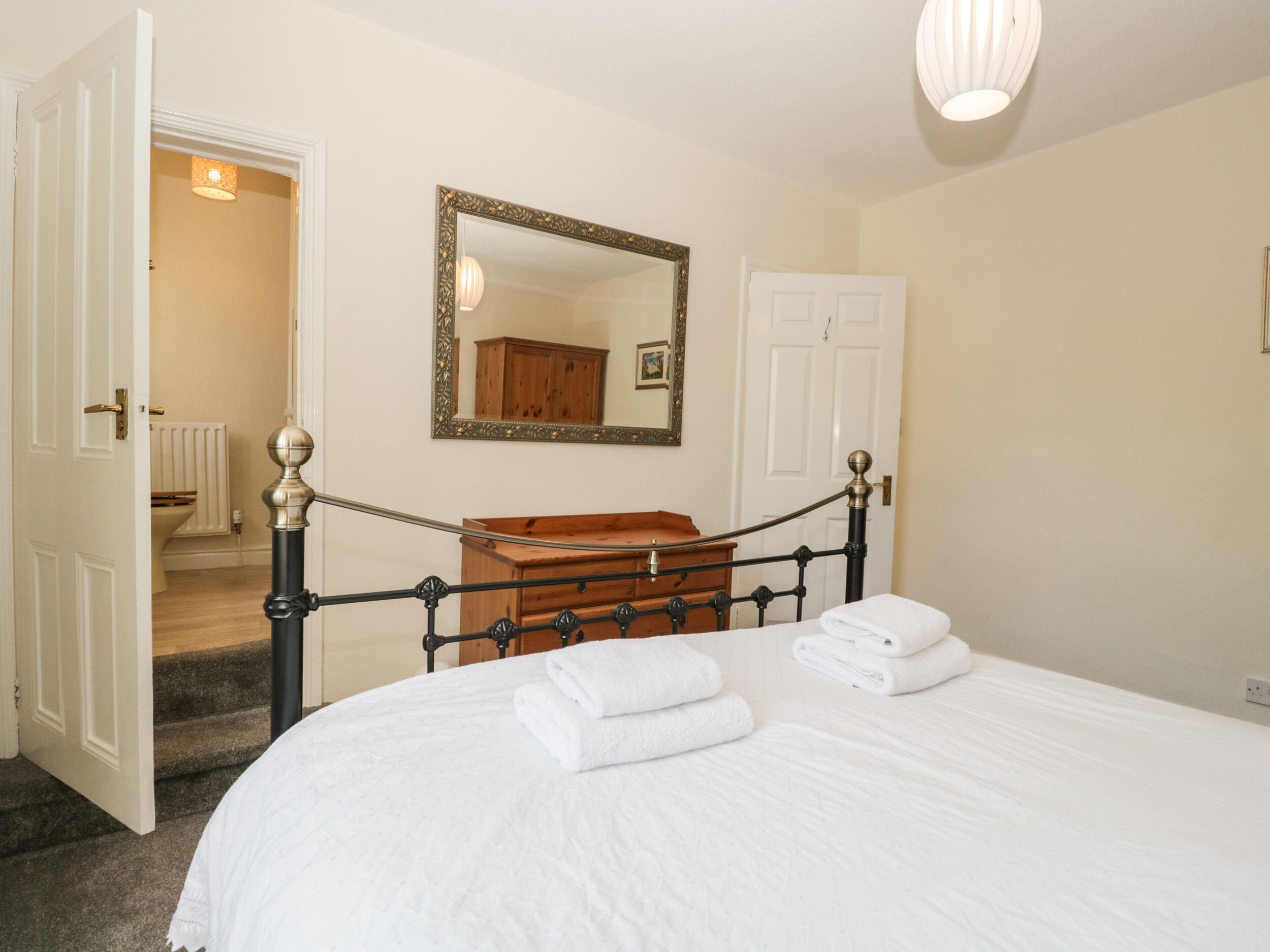 A bedroom with a bed, a dresser, a mirror, and a door leading to a bathroom.