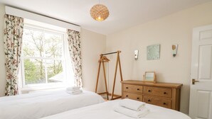 Un dormitorio con dos camas, un aparador de madera, un perchero y una ventana con cortinas.