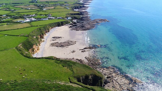 An aerial view of a coastal area with a sandy beach, rocky shoreline, and green fields. - Bwthyn Y Bae (Holyhead)