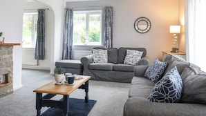 A modern living room with a grey sofa, a wooden coffee table, and a stone fireplace. - Bwthyn Y Bae (Holyhead)