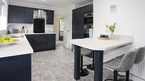 A modern kitchen with dark cabinets, a white countertop, and a grey tiled floor. - Bwthyn Y Bae (Holyhead)