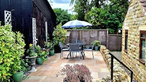 A patio area with stone flooring, potted plants, a table with chairs, and a wooden fence. - Farm Yard Cottage (Pickering)