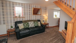 A living room with a black leather sofa, a wooden staircase, and plaid wallpaper. - Farm Yard Cottage (Pickering)