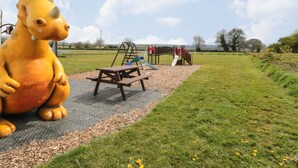 A playground with a large dinosaur sculpture, picnic table, and swings. - Farm Yard Cottage (Pickering)