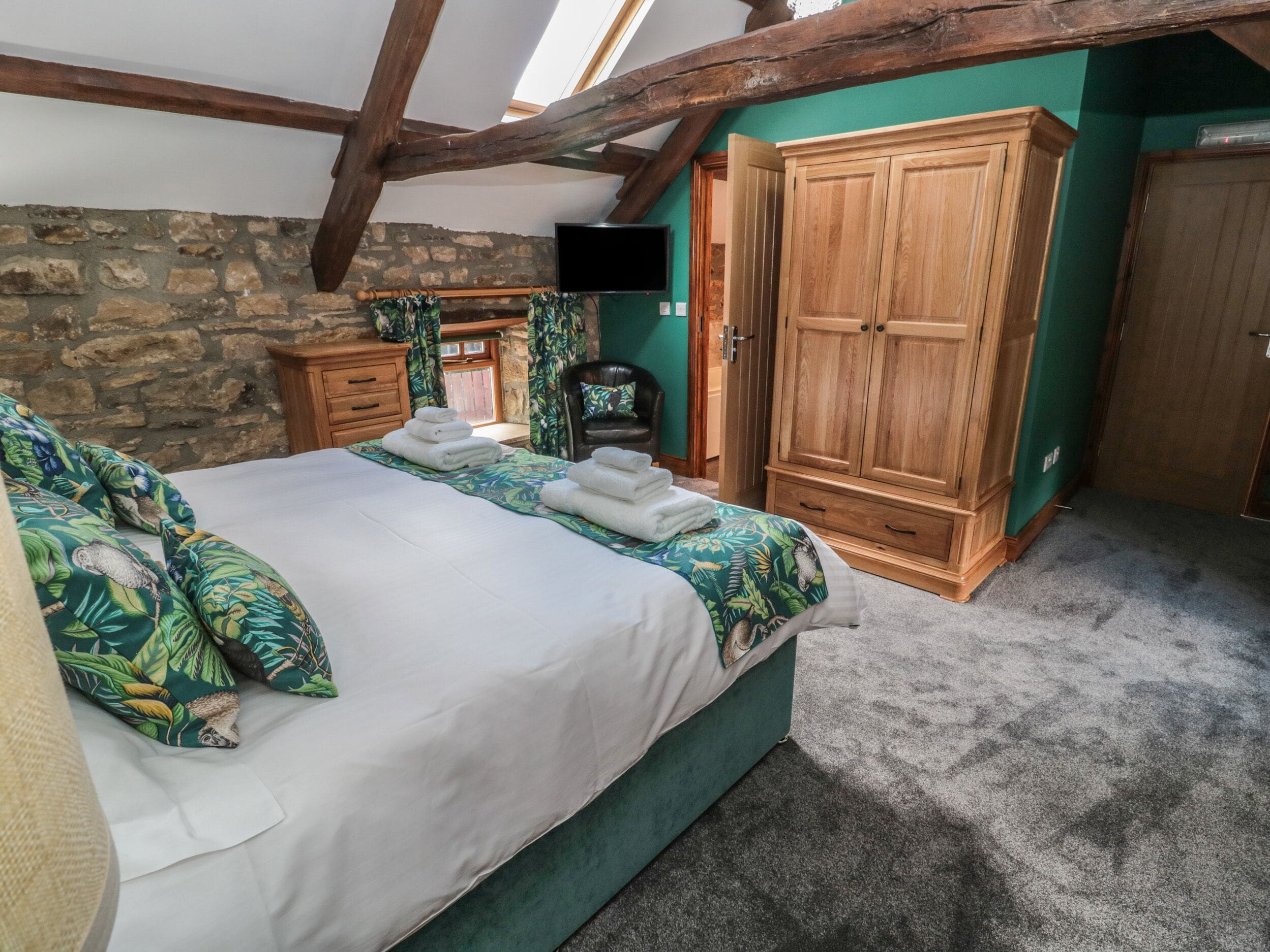 A bedroom with a large bed, wooden wardrobe, stone wall, and a television on the wall.