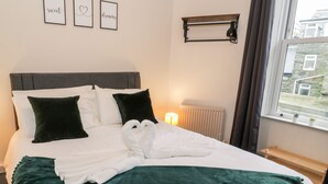 A neatly made bed with white linens, a green throw blanket, and two white towels arranged in a heart shape. - Emerald Suite (Barmouth)
