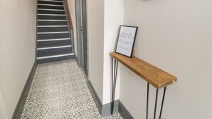 A hallway with a patterned floor, a wooden console table with a framed welcome sign, and a mirror on the wall. - Emerald Suite (Barmouth)
