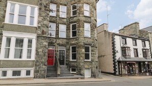 A corner building with a red door, multiple windows, and a stone facade. - Emerald Suite (Barmouth)