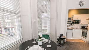 A dining area with a round table set for four, a green chair, and a view of the kitchen in the background. - Emerald Suite (Barmouth)
