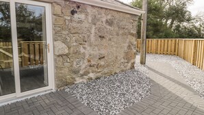 A stone exterior wall with a glass door and a wooden deck.
