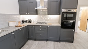 A modern kitchen with grey cabinets, a built-in oven, a microwave, and a gas stove.