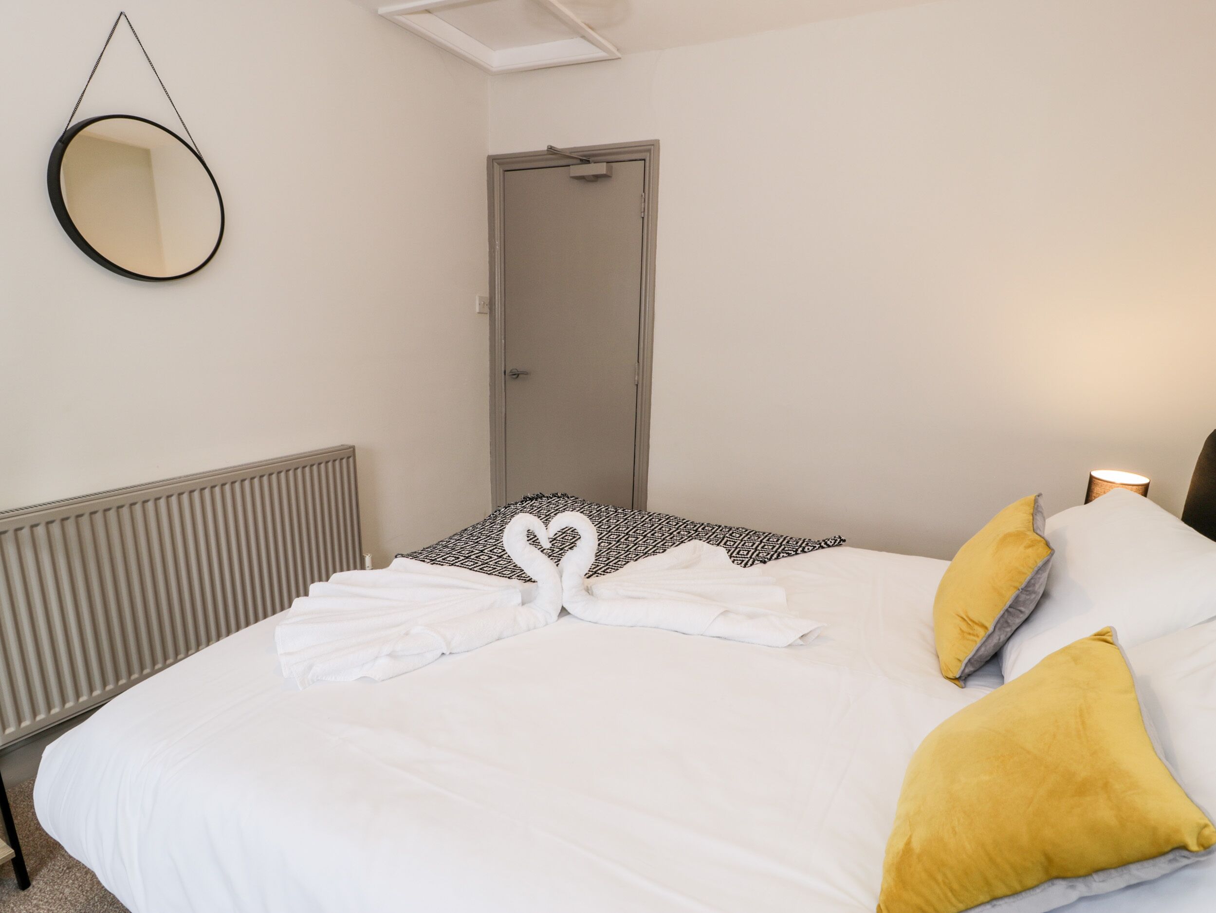 A hotel room with a bed, a round mirror, a door, and a radiator.