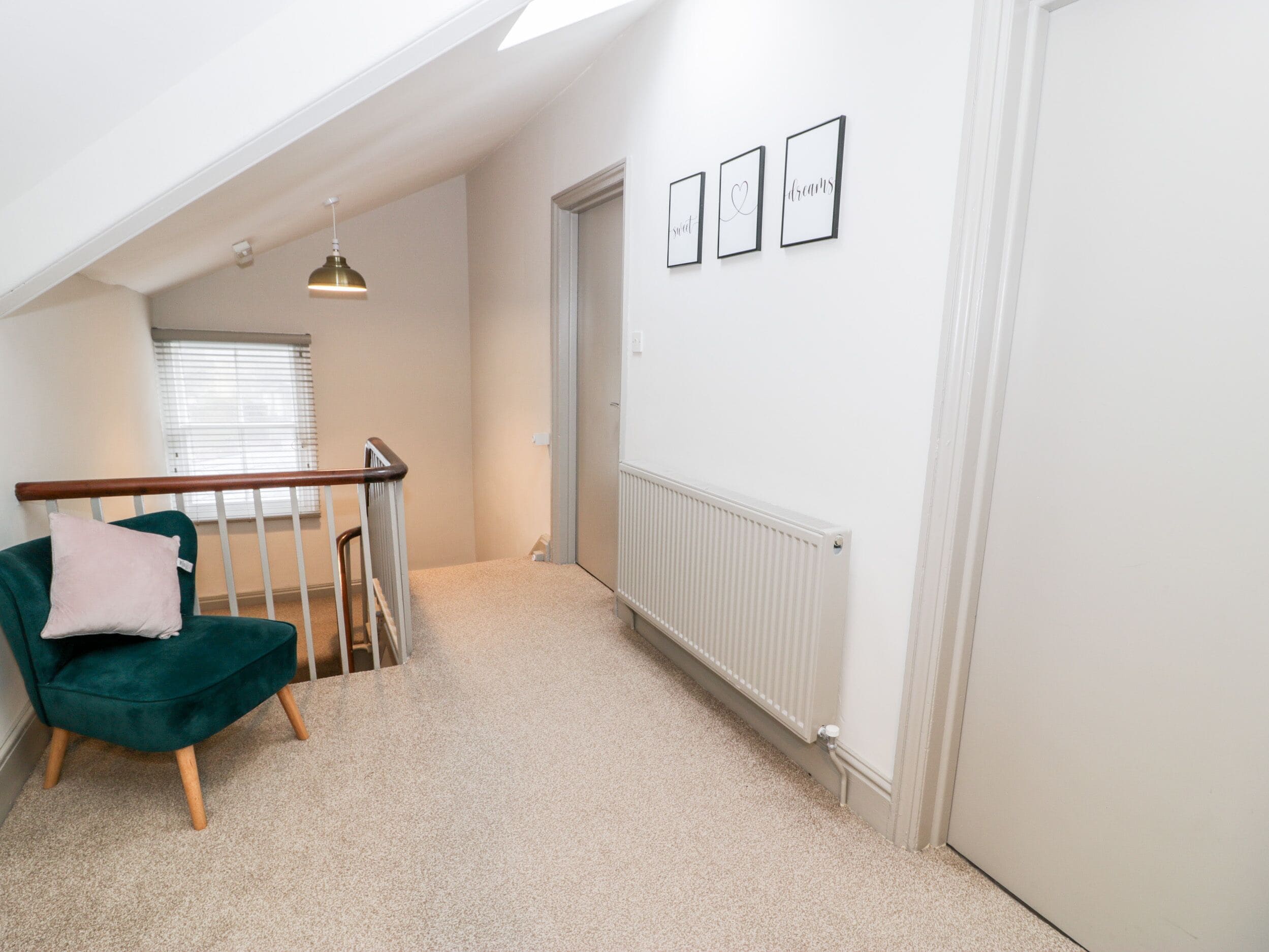 A room with a staircase, a green chair, a radiator, and framed pictures on the wall.
