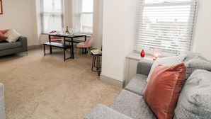 Ein modernes Wohnzimmer mit einem grauen Sofa, einem Esstisch mit Stühlen und einer kleinen Küchenzeile.