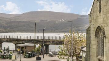 A stone bridge over a river, a church, and a parking area with trash bins.