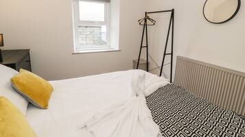 A bedroom with a bed, a window, a radiator, and a hanging mirror.
