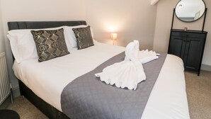 Ein ordentlich bezogenes Bett mit einer gesteppten grauen Tagesdecke, weißen Kissen und einem weißen Bademantel, der darübergelegt ist.