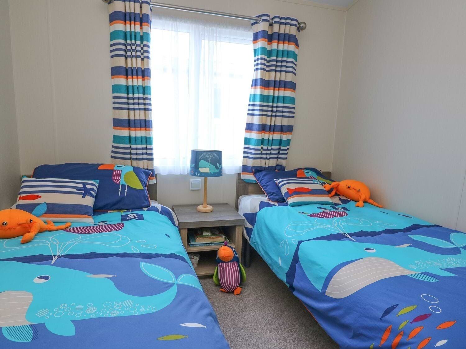 Habitación ideal para niños, con dos camas, cortinas a rayas y ropa de cama con motivos marinos.